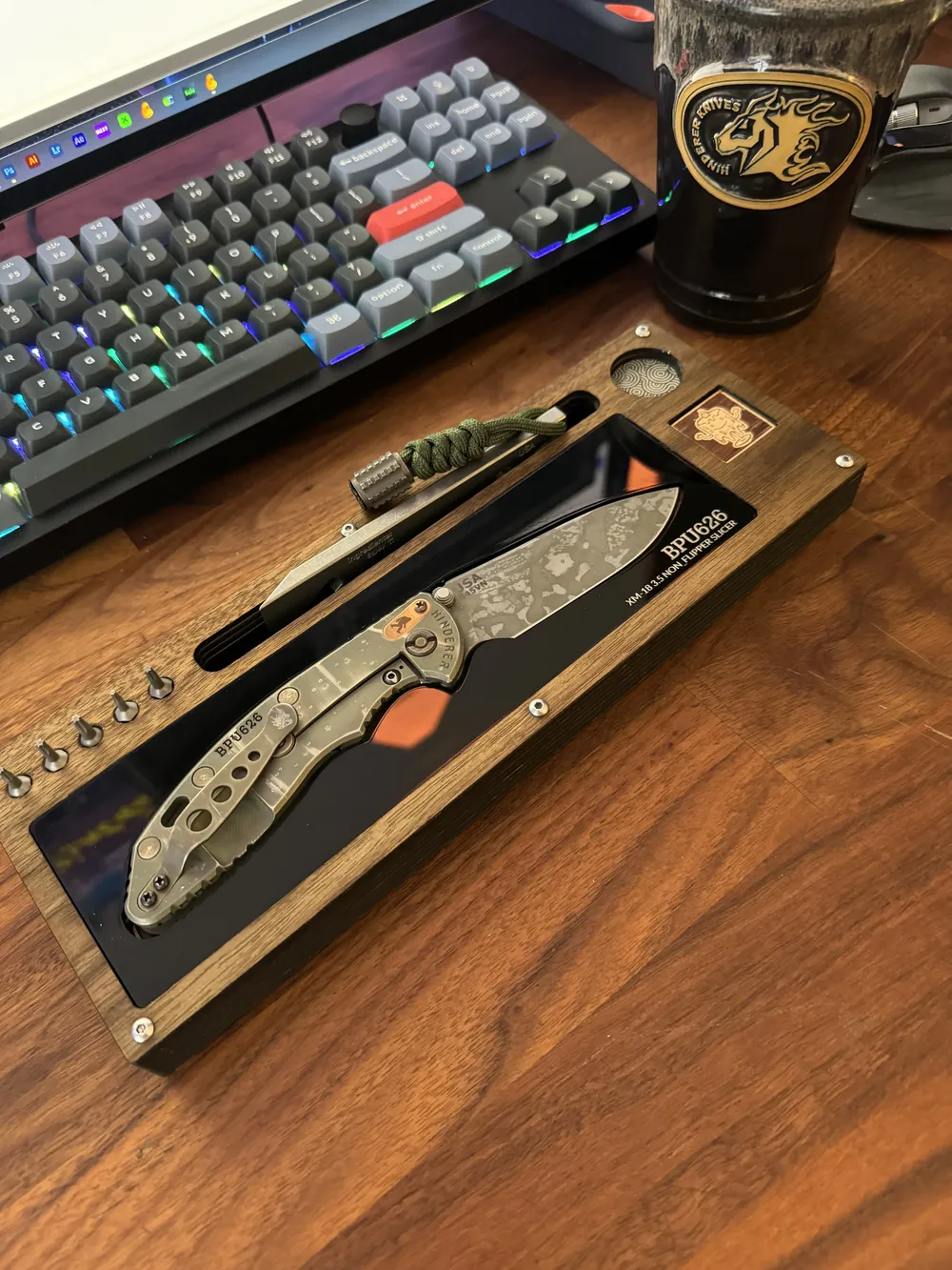 Layer Cake holding a BPU626 folder on a walnut desk in front of a backlit keyboard and a Hinderer mug
