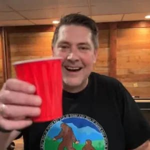 Scott of USA Made Blade, grinning and raising a red cup in a Sasquatch shirt